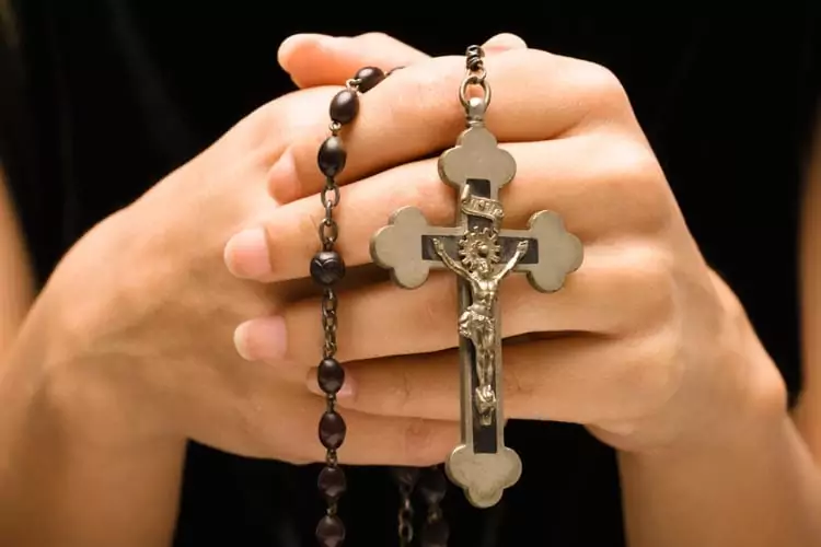 Mãos de uma moça rezando o rosário